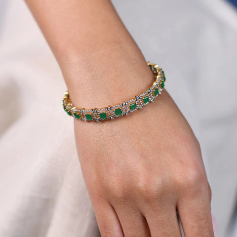 A view of an Emerald female bangle of size 2.5 is a masterpiece of luxury, featuring 3.5 carats of lab-grown diamonds. The bangles are secured through a spring lock. This stunning bangle combines the brilliance of diamonds with the rich green of emeralds, set in an exquisite two-tone design. The contrast between the metals enhances the vivid colours of the gemstones, with a total weight being 15.55 grams. Photographed on a model's hand showcases the intricate craftsmanship of the bangle 
