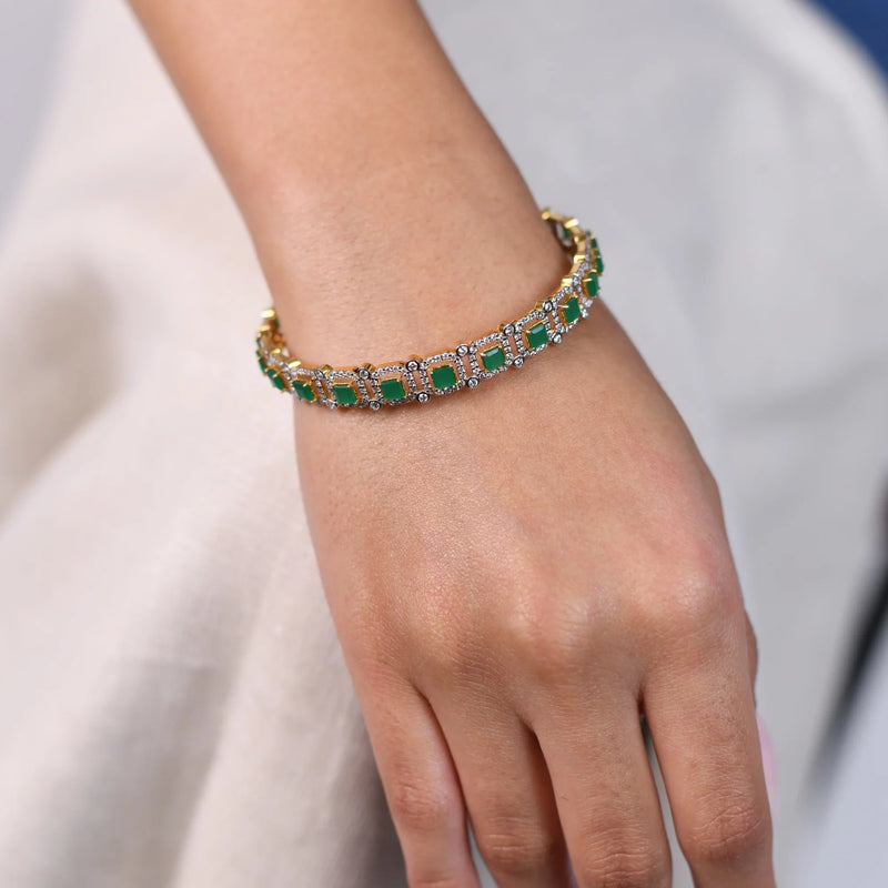 A view of an Emerald female bangle of size 2.5 is a masterpiece of luxury, featuring 3.5 carats of lab-grown diamonds. The bangles are secured through a spring lock. This stunning bangle combines the brilliance of diamonds with the rich green of emeralds, set in an exquisite two-tone design. The contrast between the metals enhances the vivid colours of the gemstones, with a total weight being 15.55 grams. Photographed on a model's hand showcases the intricate craftsmanship of the bangle 