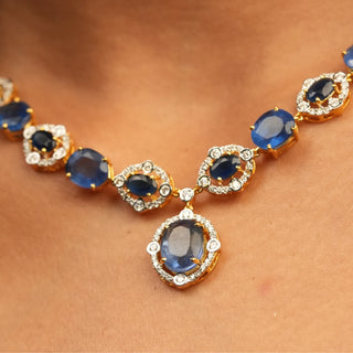 A front view of the female necklace, on a white background, showcasing a 14 KT yellow gold necklace secured with a spring lock of size 16  featuring a symmetrical pattern of lab-grown blue Sapphires with a total product weight of 29.406 grams in a diamond-studded setting with a total of 2.37 carat finished with a central blue Sapphire hanging at the bottom creating a classy look for any occasion.