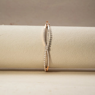 Front view of a diamond bracelet in 14 KT Dual Gold, featuring intertwined pavé-set diamond strands crossing at a floral diamond cluster, displayed against a soft beige backdrop.
