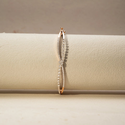 Front view of a diamond bracelet in 14 KT Dual Gold, featuring intertwined pavé-set diamond strands crossing at a floral diamond cluster, displayed against a soft beige backdrop.
