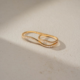 Top view of an infinity diamond band in 14 KT Yellow Gold, featuring intertwined wave-inspired bands adorned with pavé-set round lab-grown diamonds in a graceful crossover design, displayed against a beige backdrop.
