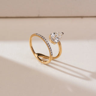 Angled view of Floating Pear Bypass Diamond Ring in yellow gold, featuring a pear-shaped lab-grown diamond set in a bypass design with pavé diamond accents along one band, displayed on a beige backdrop.