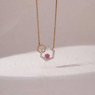 Front view of geometric hexagon pendant necklace in yellow gold, featuring an open hexagon with pavé lab-grown diamonds and a smaller pink stone cluster centre. Suspended on a fine chain against a soft beige backdrop.
