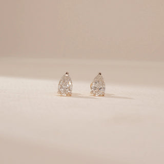 Front view of diamond stud earrings in 14KT Yellow Gold, featuring pear-shaped diamonds on a beige backdrop.