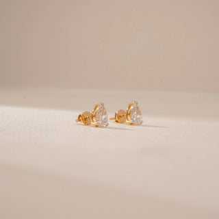 Side view of diamond stud earrings in 14KT Yellow Gold, featuring pear-shaped diamonds on a beige backdrop.