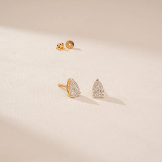 Angled view of diamond stud earrings in 14KT Yellow Gold, featuring pear-shaped diamonds on a beige backdrop.
