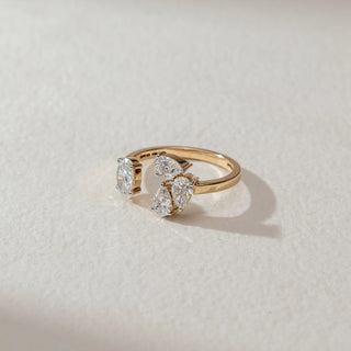 Top view of multi-stone diamond ring in yellow gold, featuring oval and pear-shaped lab-grown diamonds in a clustered open setting. Placed on a textured beige surface, the design casts a soft shadow.