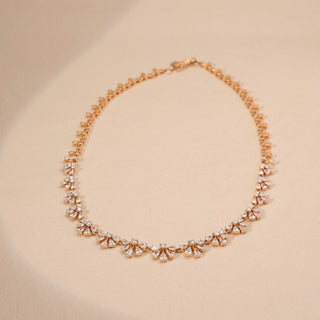 Top view of a floral lab-grown diamond necklace in 18KT Rose Gold, featuring marquise and pear-shaped diamond clusters in a continuous design. Captured against a beige backdrop, the elegant silhouette radiates brilliance.