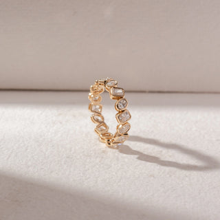 Angled view of eternity band in yellow gold with mixed-shape diamonds in bezel settings, set on a soft neutral background, highlighting structured design and continuous, radiant sparkle.