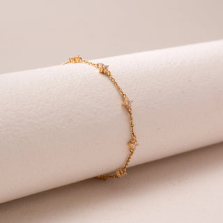 Angled view of a delicate gold chain bracelet, featuring floral diamond accents spaced along the chain. Captured against a soft beige backdrop, the design reflects minimal elegance and refined sparkle.
