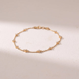 Top view of a delicate gold chain bracelet, featuring floral diamond accents spaced evenly along the chain. Captured against a soft beige backdrop, the design reflects minimal elegance and refined sparkle.