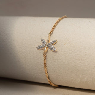 Close Up view of a dragonfly-inspired diamond bracelet in 14 KT Yellow Gold, featuring marquise-shaped diamond wings on a delicate chain, displayed against a soft beige backdrop.