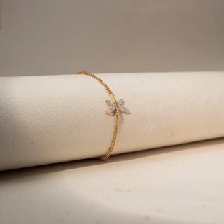 Side view of a dragonfly-inspired diamond bracelet in 14 KT Yellow Gold, featuring marquise-shaped diamond wings on a delicate chain, displayed against a soft beige backdrop.