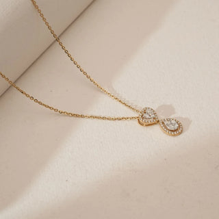 Angled view of yellow gold heart and teardrop diamond pendant necklace featuring pavé-set round lab grown diamonds with a pear-shaped centre stone, resting on a soft beige textured surface.