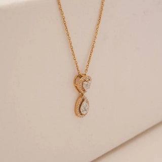Side view of yellow gold heart and teardrop diamond pendant necklace with pavé-set round lab grown diamonds and pear-shaped centre stones, suspended on a delicate chain against a beige backdrop.