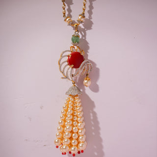 Front view of a gold pendant necklace, featuring red and green gemstones with diamond accents and cascading pearl tassels. Captured against a soft pink backdrop, the design reflects regal elegance and artistry.
