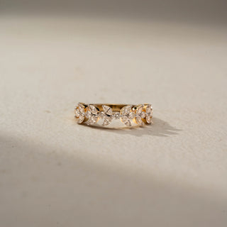 Front view of a diamond eternity band in 14 KT Yellow Gold, featuring marquise-cut and round lab-grown diamonds arranged in a delicate leaf-inspired pattern, displayed against a beige backdrop.