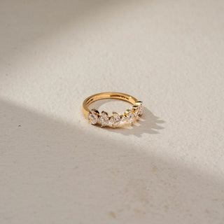 Side view of a diamond eternity band in 14 KT Yellow Gold, featuring marquise-cut and round lab-grown diamonds arranged in a delicate leaf-inspired pattern, displayed against a beige backdrop.