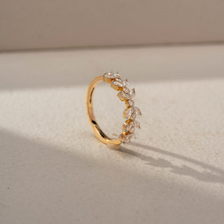 Angled view of a diamond eternity band in 14 KT Yellow Gold, featuring marquise-cut and round lab-grown diamonds arranged in a delicate leaf-inspired pattern, displayed against a beige backdrop.