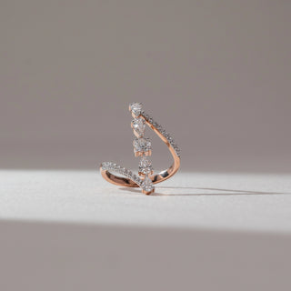  Side angle view of geometric diamond ring in rose gold, featuring a central round lab-grown diamond with vertically set pear-shaped stones and pavé arms. Placed on a neutral backdrop, the design reflects fluid structure and soft brilliance