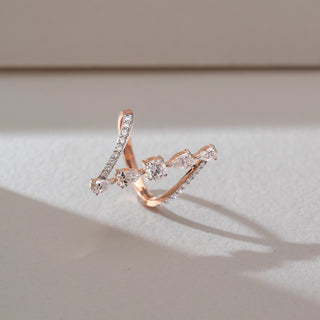 Top angle view of geometric diamond ring in rose gold, featuring a central round lab-grown diamond with pear-shaped side stones and pavé-set arms. Placed on a soft neutral surface, the design highlights fluid curves and radiant sparkle.