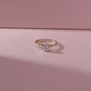 Top view of round diamond solitaire ring in white gold with a slim band, set on a soft pink textured surface, highlighting classic design and delicate, radiant sparkle.
