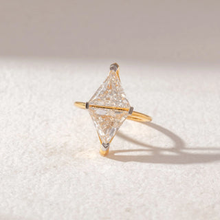 Top view of Kite-Shaped Diamond Solitaire Ring in 14KT Yellow Gold, featuring a horizontally set kite-cut center diamond with minimal prongs. Set on a soft beige surface, it reflects modern brilliance.
