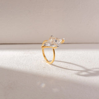 Angled side view of Kite-Shaped Diamond Solitaire Ring in 14KT Yellow Gold, featuring a kite-cut center diamond in a sleek prong setting. Set on a soft beige surface, the design reflects modern elegance.
