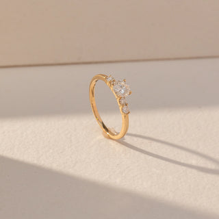 Side view of Round Three Stone Diamond Ring in 14KT Yellow Gold, featuring a centred round lab grown diamond with round side stones. Set on a beige backdrop, the design highlights depth and classic elegance.
