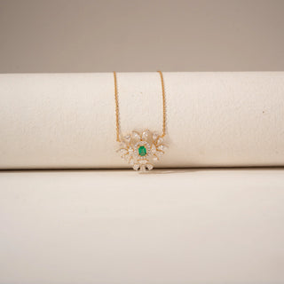 Close-up view of a green gemstone diamond pendant in 14KT Yellow Gold, featuring a floral cluster design against a beige backdrop.