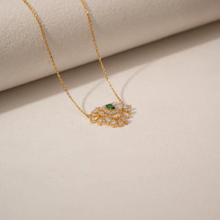 Top view of a green gemstone diamond pendant in 14KT Yellow Gold, featuring a floral cluster design against a beige backdrop.