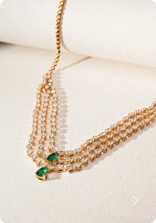 Luxury 18KT hallmarked yellow gold necklace featuring 8.19-carat EF color VVS clarity lab-grown diamonds and 1.095-carat pear-shaped emeralds, weighing 24.687 grams, 16 inches in length, elegantly displayed on a beige surface — priced at INR 632,325.