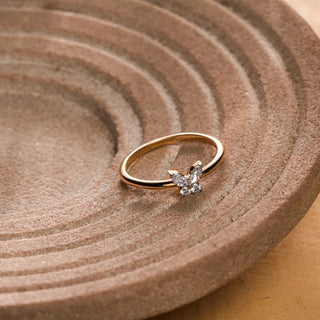 Slim yellow gold ring adorned with a petite butterfly motif set in marquise and round diamonds, resting on a textured circular stone surface.