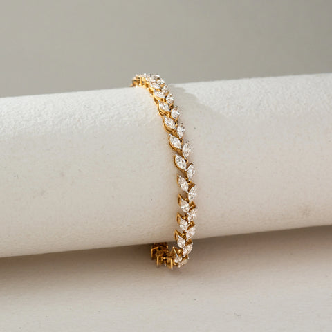 Side view of Marquise Diamond Tennis Bracelet in 14KT Yellow Gold, featuring a continuous row of marquise-shaped lab grown diamonds in prong setting. Placed on a beige backdrop, the design highlights fluid elegance and brilliance.
