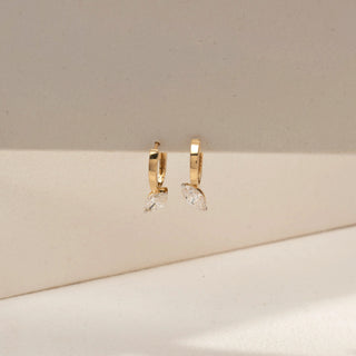 Front view of marquise solitaire drop earrings in 14 KT Dual Gold, featuring marquise-cut lab-grown diamonds suspended from sleek huggie hoops, displayed against a beige backdrop.