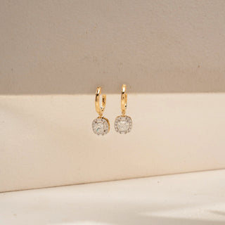 Front view of cushion halo drop earrings in 14 KT Yellow Gold, featuring cushion-cut lab-grown diamonds framed by sparkling halo settings, suspended from sleek huggie hoops against a beige backdrop.