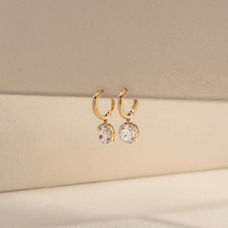 Side view of cushion halo drop earrings in 14 KT Yellow Gold, featuring cushion-cut lab-grown diamonds framed by sparkling halo settings, suspended from sleek huggie hoops against a beige backdrop.