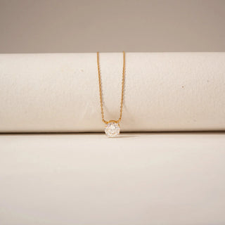 Close-up view of a round diamond pendant in 14KT Yellow Gold, featuring a solitaire stone in a delicate setting against a beige backdrop.