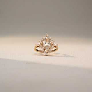 Front view of a floral-inspired diamond ring in 14KT Yellow Gold, featuring a marquise-cut centre stone with clustered accent diamonds. Captured against a beige backdrop, it radiates elegant sparkle.