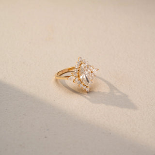 Side view of a floral-inspired diamond ring in 14KT Yellow Gold, featuring a pear-cut centre stone encircled by marquise and round accent diamonds. Captured against a beige backdrop, it radiates elegant sparkle.