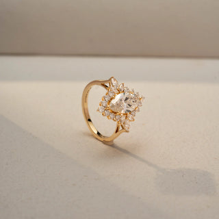 Angled view of a floral-inspired diamond ring in 14KT Yellow Gold, featuring a marquise-cut centre stone framed by clustered accent diamonds. Captured against a beige backdrop, it radiates elegant sparkle.