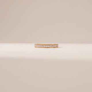 Front view of a diamond eternity band in 14KT Yellow Gold, featuring a continuous row of round diamonds with beaded gold edges on a beige backdrop.