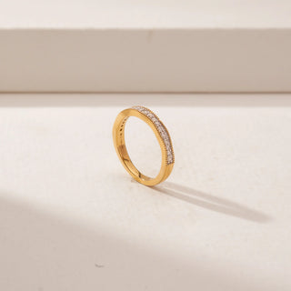 Angled view of a diamond eternity band in 14KT Yellow Gold, featuring a continuous row of round diamonds with beaded gold edges on a beige backdrop.