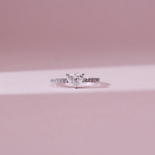 Front view of Classic Heart Solitaire Diamond Ring in 14KT White Gold, featuring a heart-shaped centre diamond in a three-prong setting with a pavé diamond band, set against a soft pink backdrop.