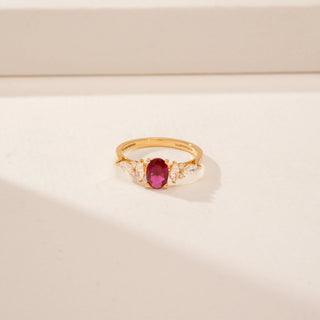 Top view of a 14KT Yellow Gold diamond ring, featuring an oval red centre stone and pear-shaped diamonds.
