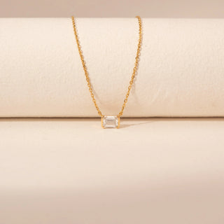 Front view of a 14KT yellow gold necklace, featuring a rectangular emerald-cut diamond pendant. Captured against a beige backdrop.