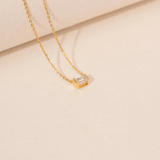 Angled view of a 14KT yellow gold necklace, featuring a rectangular emerald-cut diamond pendant. Set against a beige backdrop.