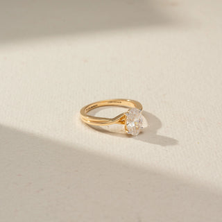 Top view of an oval-cut solitaire diamond ring featuring a twisted yellow gold band and four-prong setting, elegantly displayed on a neutral surface with soft natural lighting.