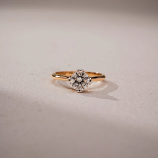 Front view of a round solitaire engagement ring in 14 KT Yellow Gold, featuring a round lab-grown diamond in a classic six-prong setting on a sleek polished band, displayed against a beige backdrop.